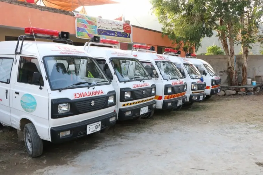 A line of five white Suzuki ambulances operated by Tanawal Welfare Organization parked outside a facility.