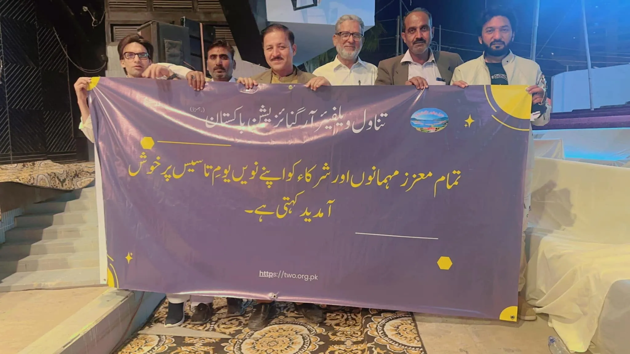 Six members holding a Tanawal Welfare Organization Pakistan banner celebrating its 9th foundation day.