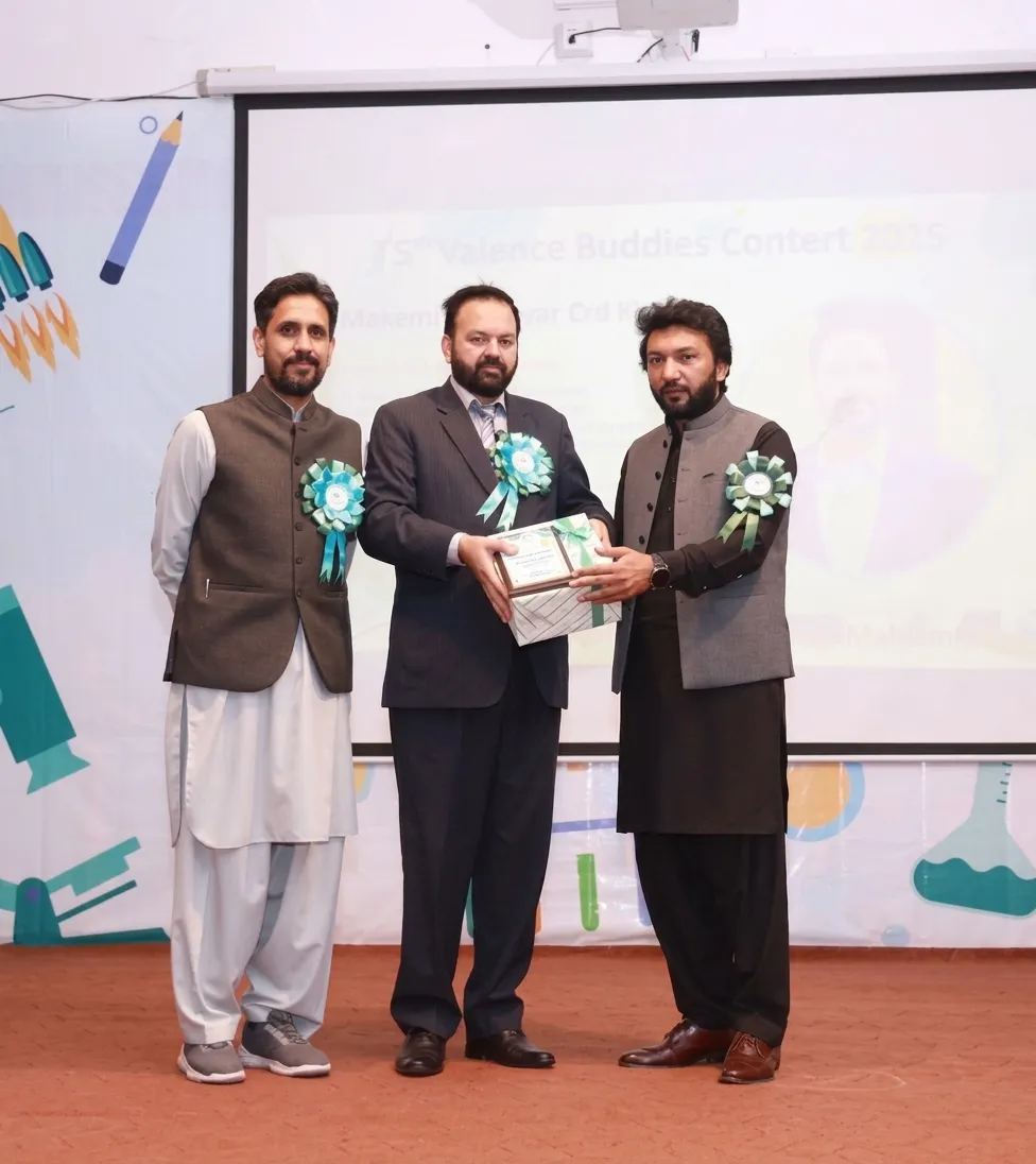 Qaiser Akash Khan receiving a wrapped gift award on stage from Prof. Dr. Ghulam Mujtaba Shah of Hazara University.